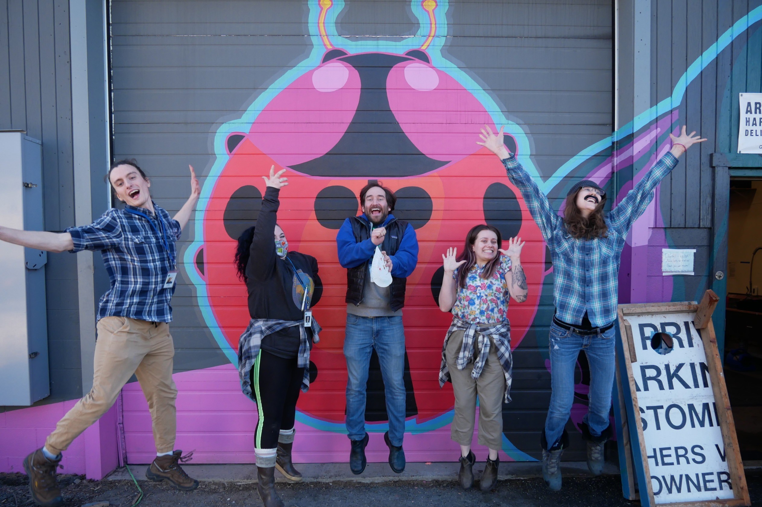 young adults jumping in front of garage door painted with ladybug mural